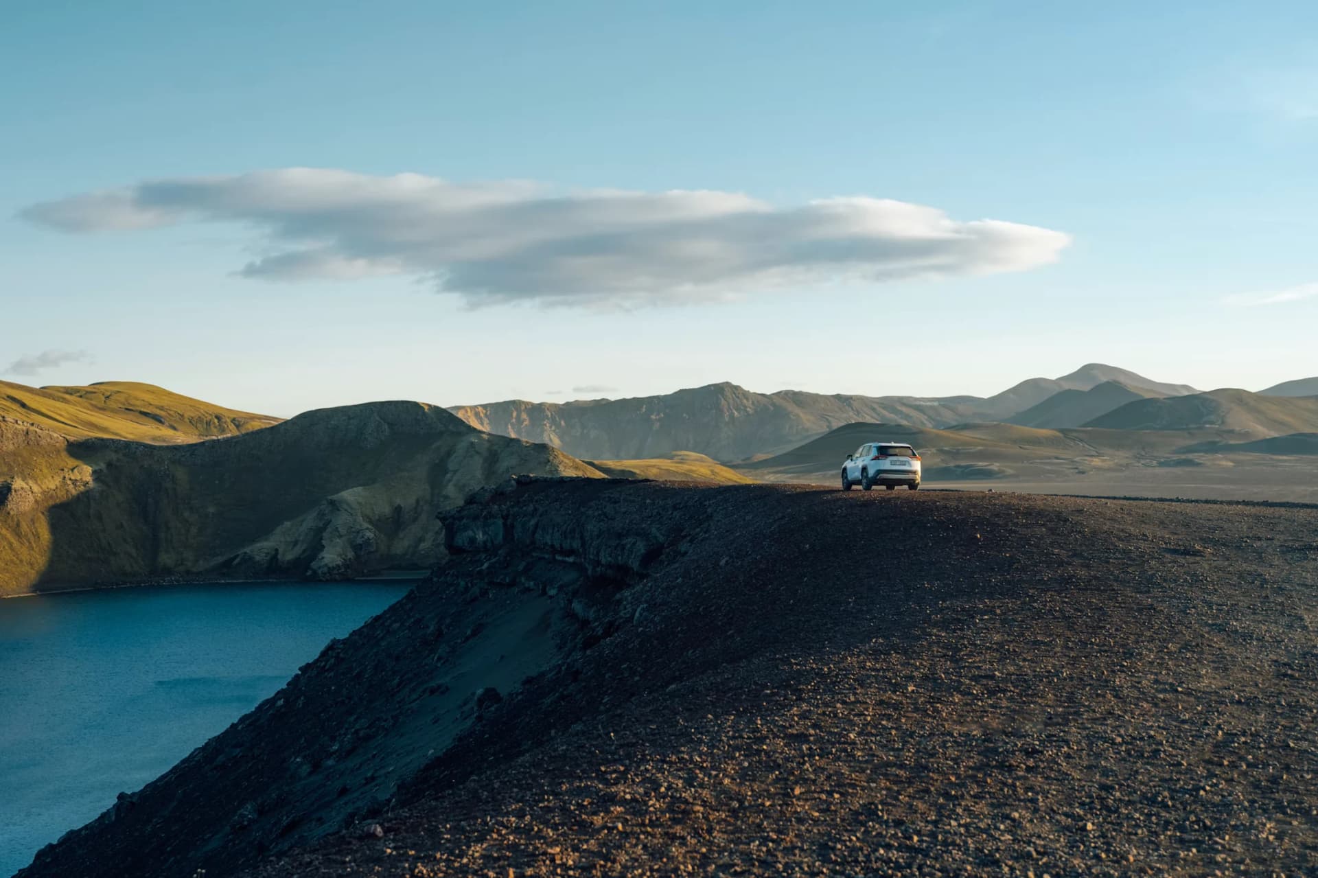 A car beside a blue lake in a volcanic Icelandic landscape