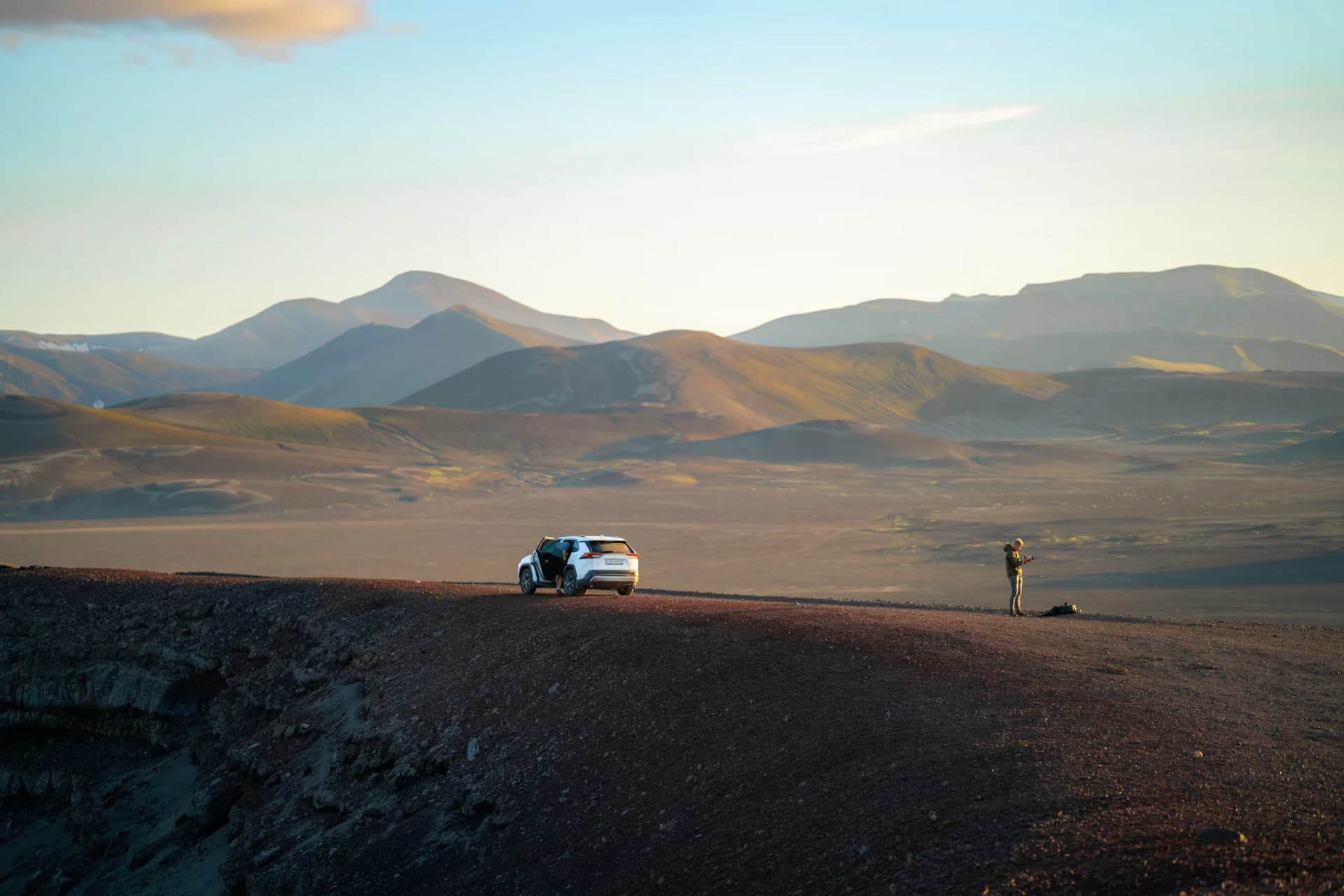 A small car and traveller among wide volcanic hills in Iceland