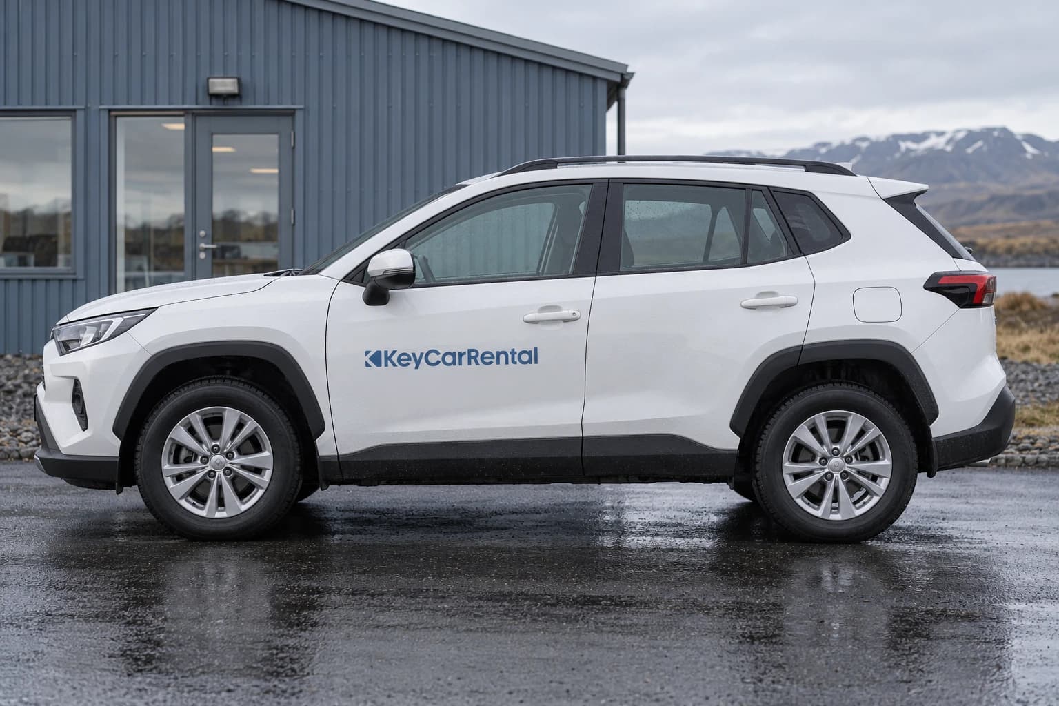 White crossover with an Atlantic blue Key Car Rental door decal outside a corrugated building