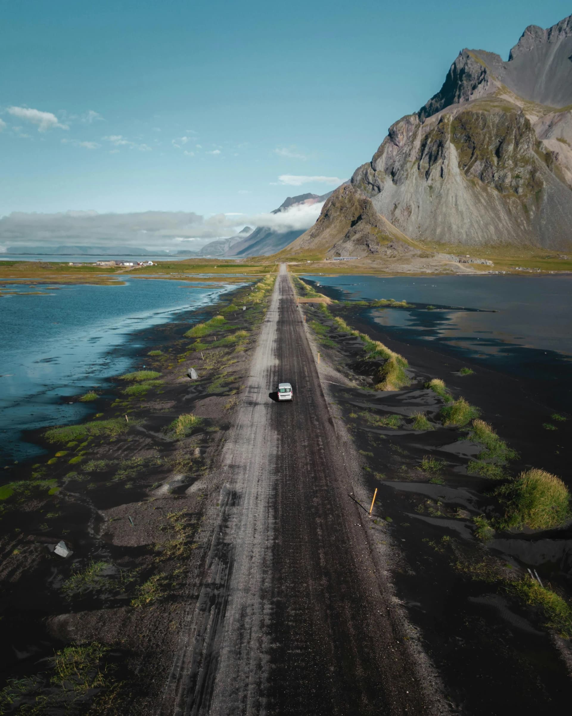 A gravel road beside water leading towards steep Icelandic mountains